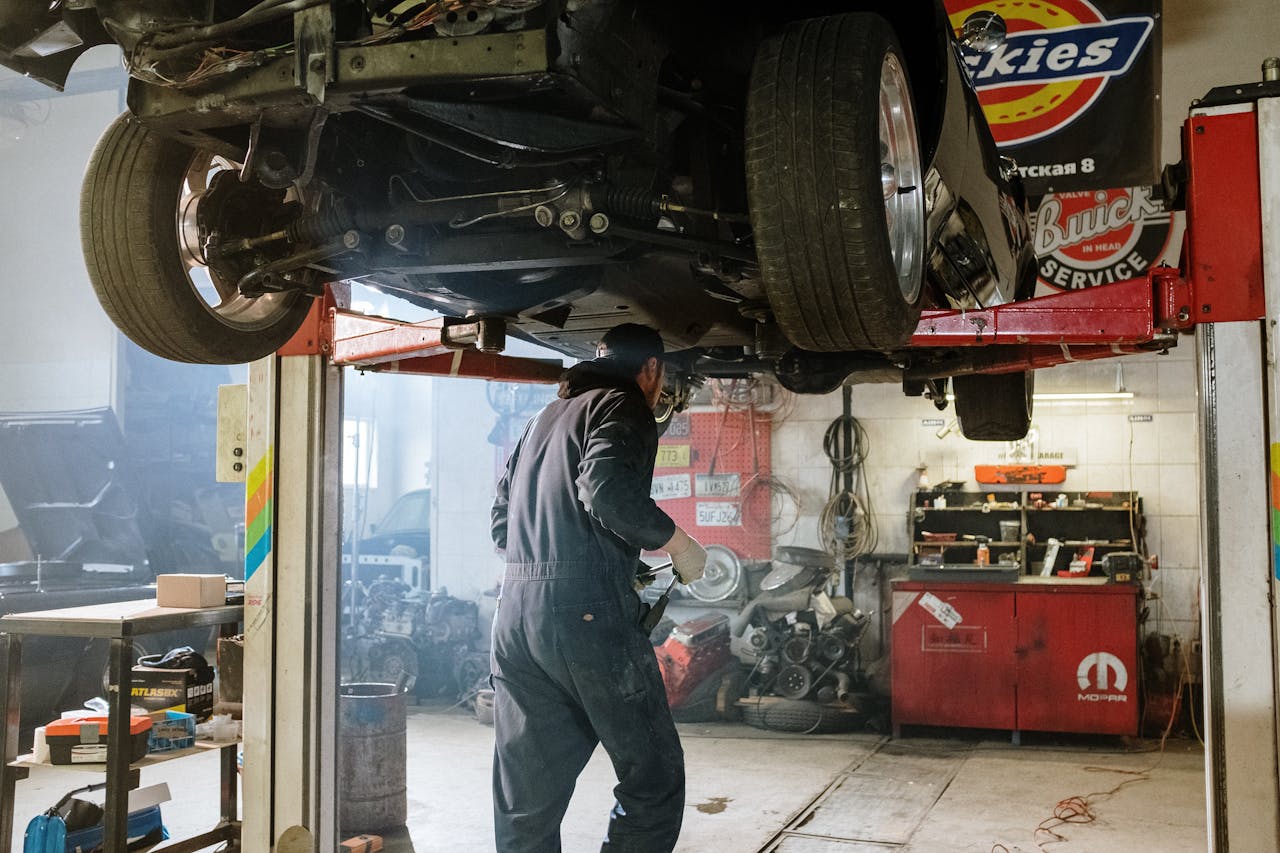 Mechanic repairing a vehicle in a busy workshop with various automotive tools.